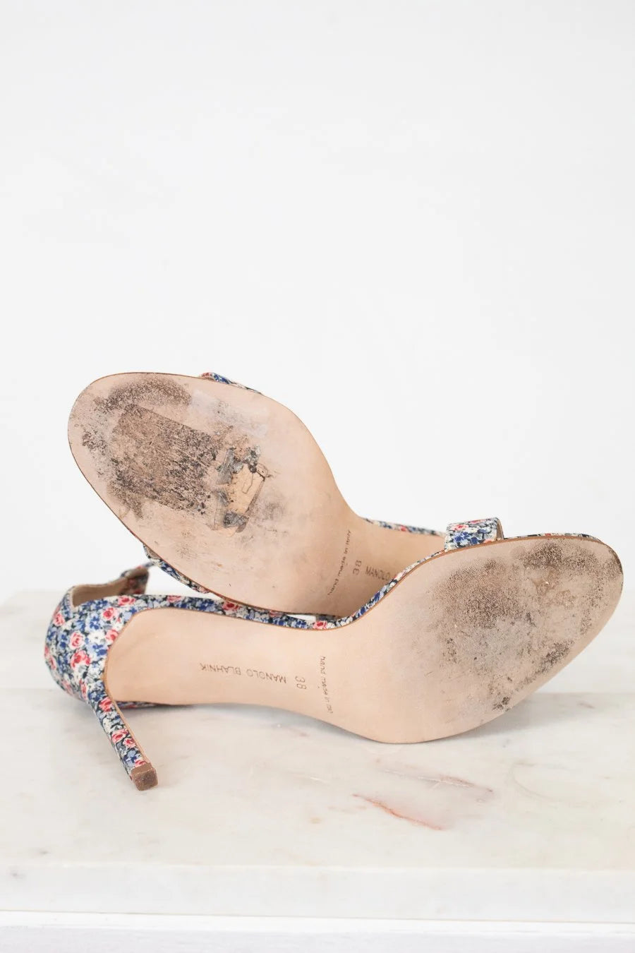 Pair of worn high-heeled shoes with floral pattern on a white background