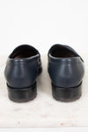 A pair of navy blue leather penny loafers shown from the back, resting on a white marble surface against a white background.