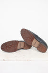 A pair of navy leather loafers shown from the bottom, displaying their brown lug soles, resting on a white marble slab against a white background.