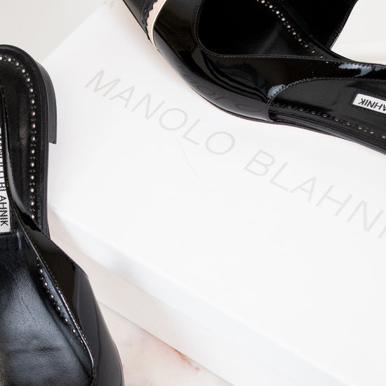 Black high-heeled shoes with 'Manolo Blahnik' branding on a white surface.
