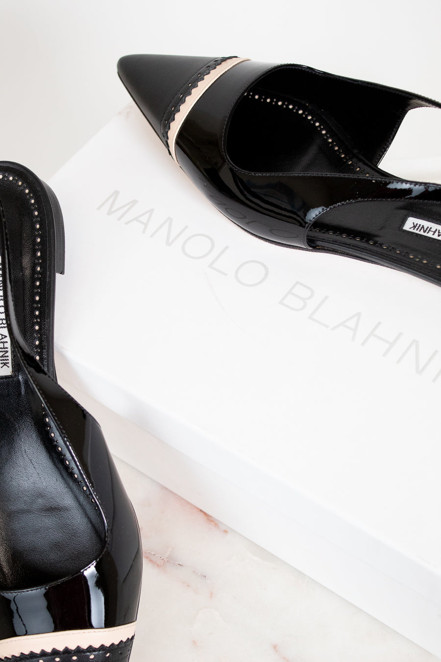 Black high-heeled shoes with 'Manolo Blahnik' branding on a white surface.