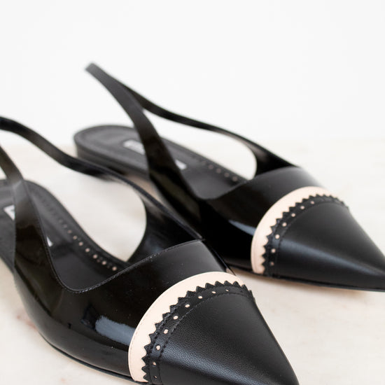 Black pointed-toe shoes with beige accents on a light background