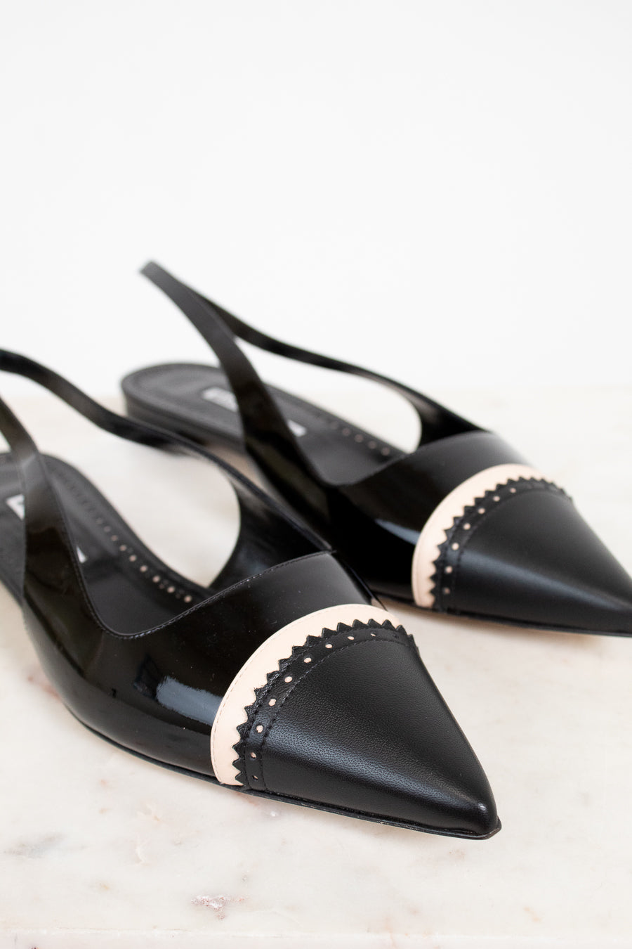 Black pointed-toe shoes with beige accents on a light background