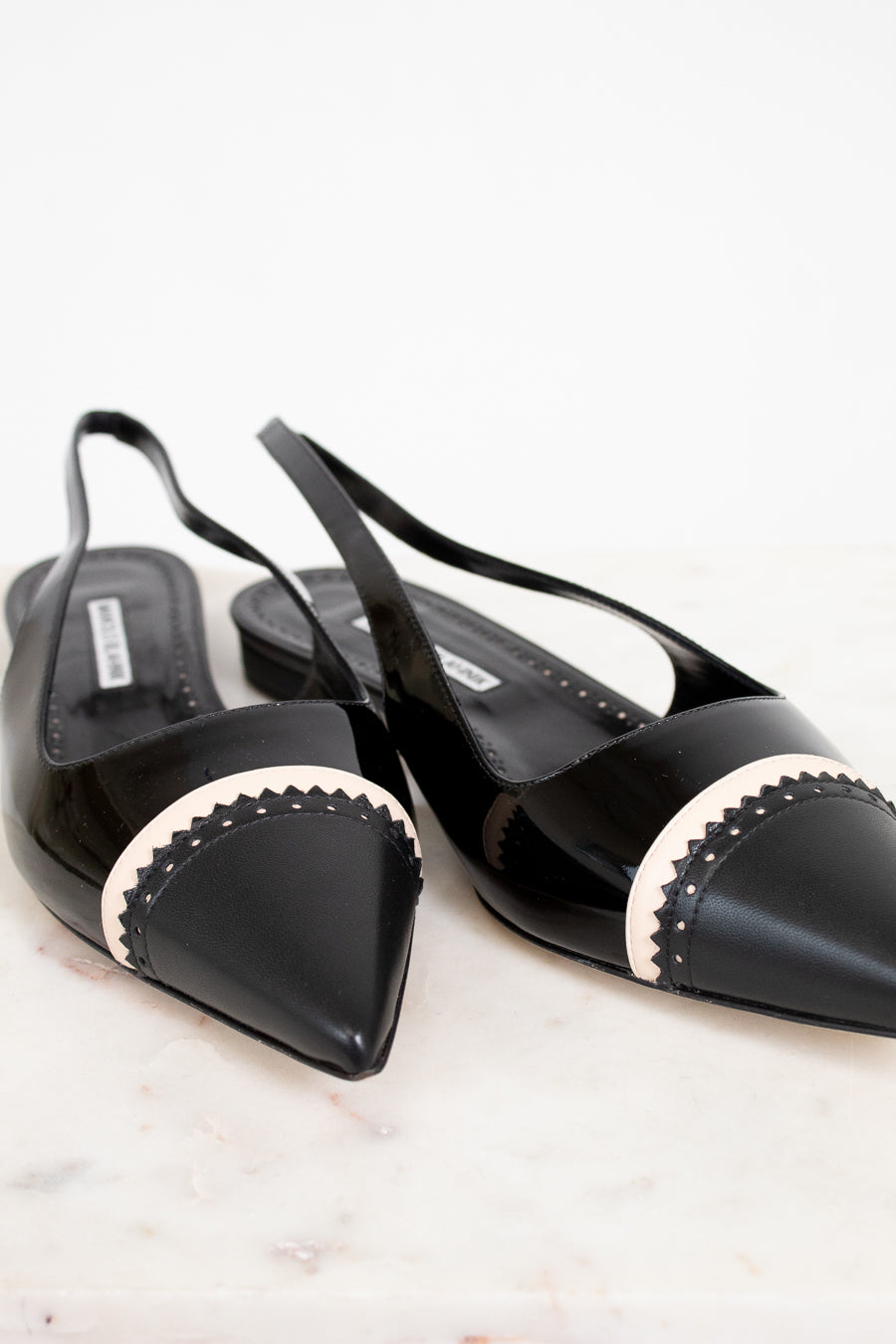 Black pointed-toe slingback shoes with white trim on a light background