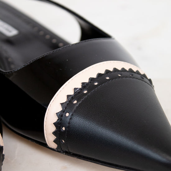 Black pointed-toe shoe with decorative band on a light background