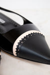 Black pointed-toe shoe with decorative band on a light background