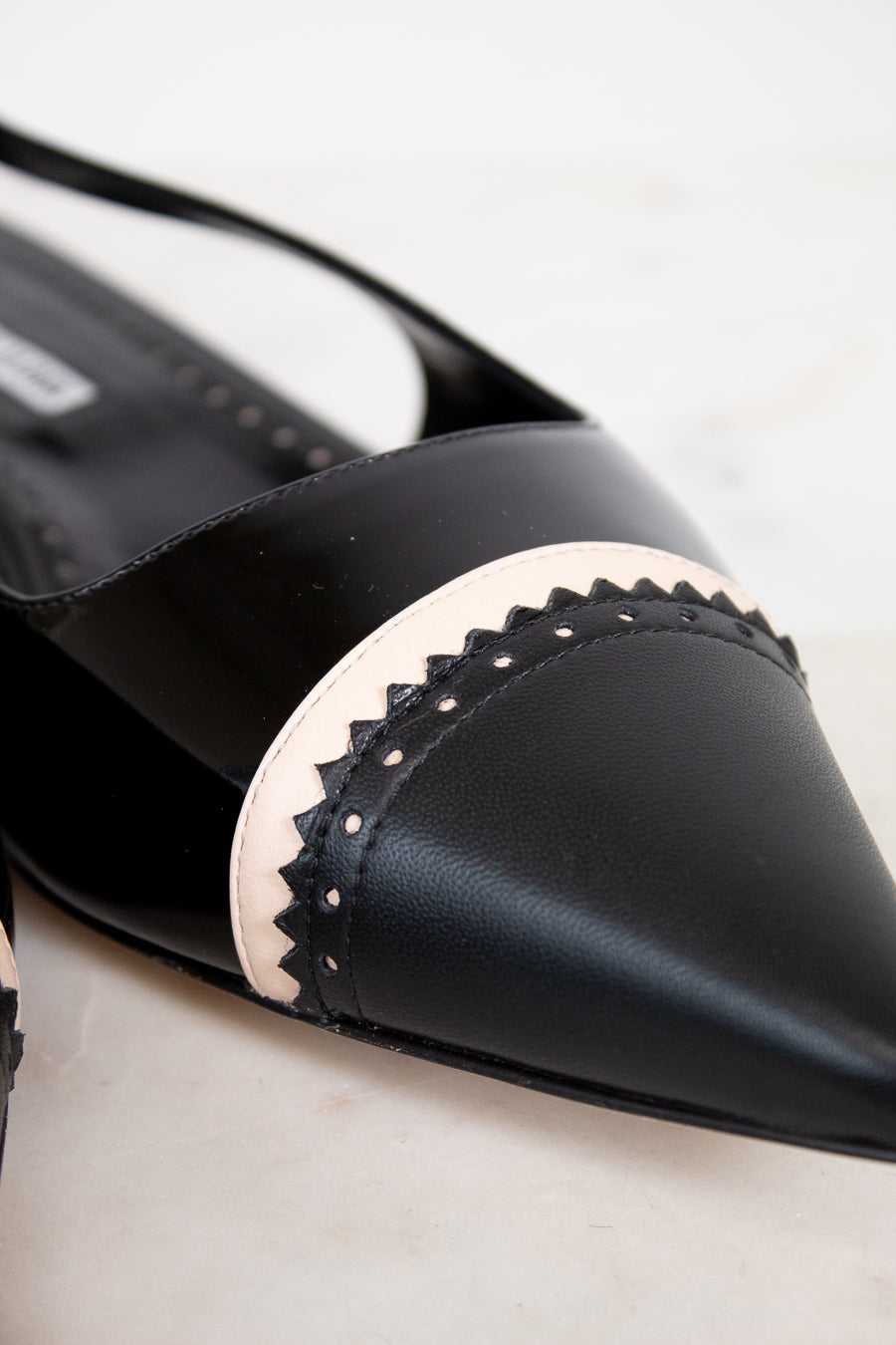 Black pointed-toe shoe with decorative band on a light background