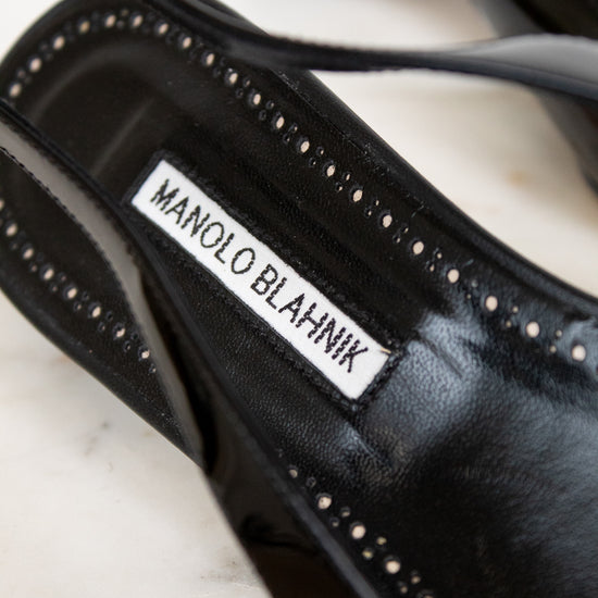 Black high-heeled shoe with 'Manolo Blahnik' label on a marble surface