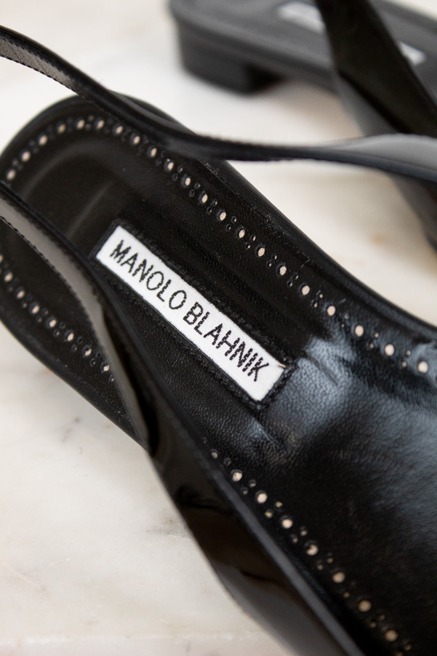 Black high-heeled shoe with 'Manolo Blahnik' label on a marble surface