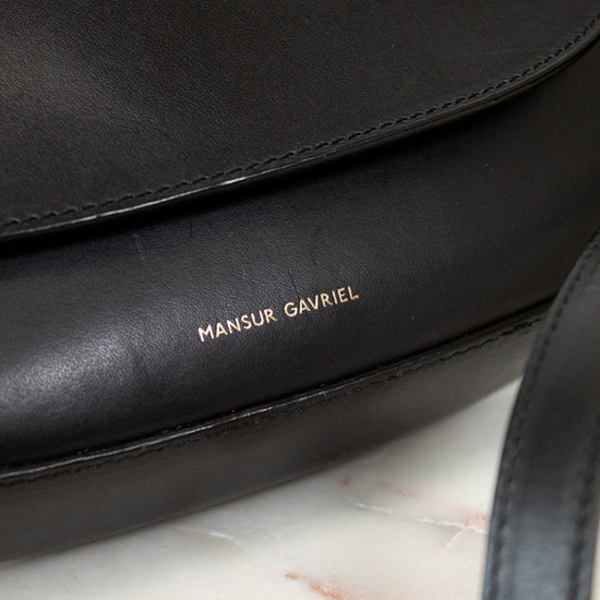 Black handbag with 'Mansur Gavriel' branding on a marble surface