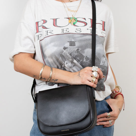 Person wearing a 'Rush' t-shirt and holding a black bag against a plain background