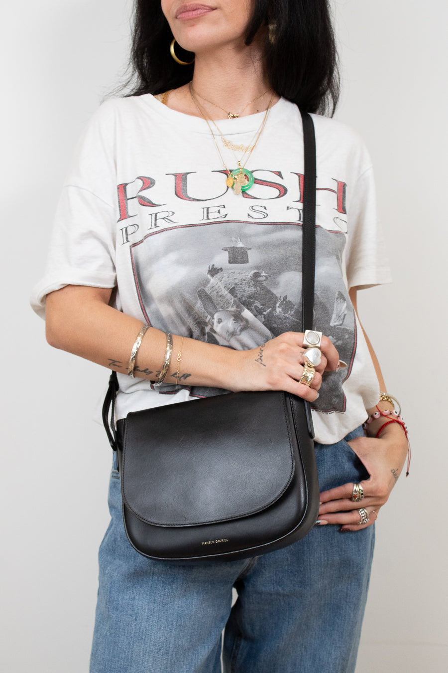 Person wearing a 'Rush' t-shirt and holding a black bag against a plain background