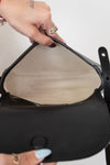 Person holding a black handbag with a neutral background