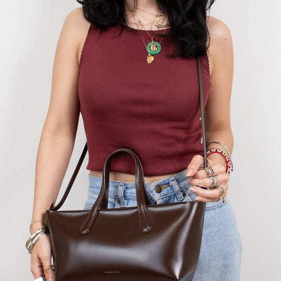 Woman holding a brown handbag against a plain background