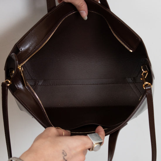 Brown leather handbag held by a person against a white background