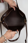 Brown leather handbag held by a person against a white background