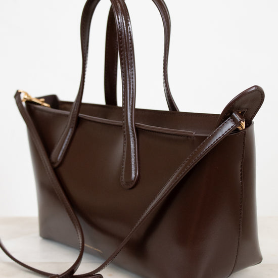 Brown leather handbag with a shoulder strap on a light background