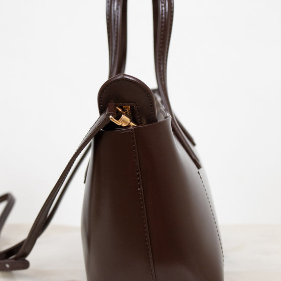 Brown leather handbag with gold clasp on a white marble surface