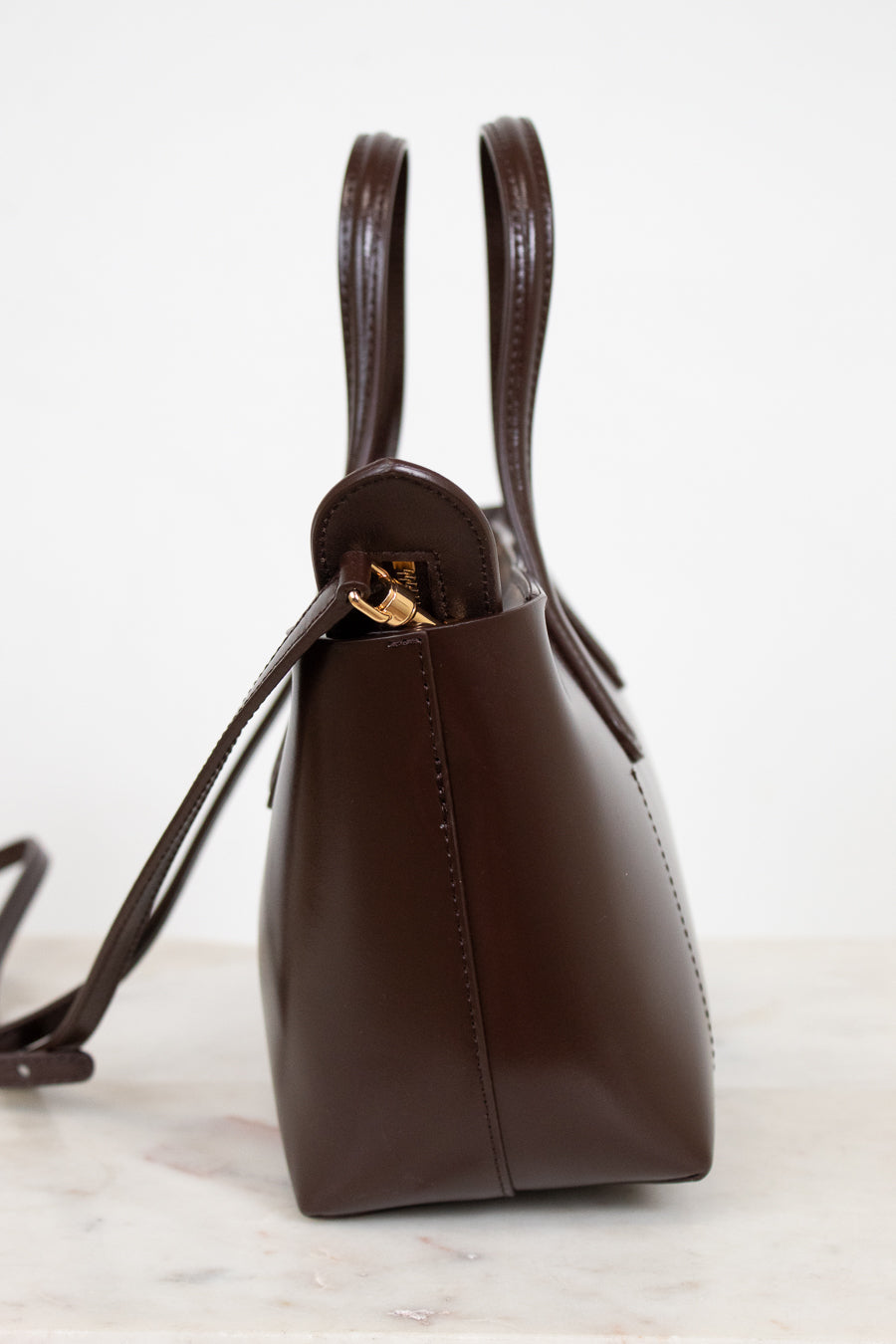 Brown leather handbag with gold clasp on a white marble surface