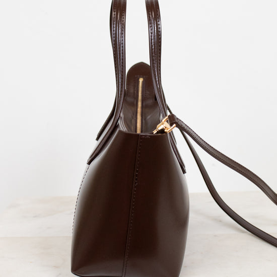 Brown leather handbag with gold clasp on a light marble surface