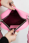 Pink handbag with a visible brand logo, held open by hands against a neutral background