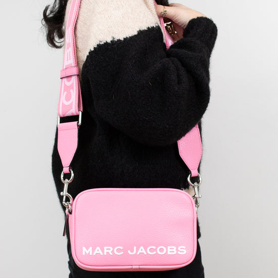 Person wearing a pink Marc Jacobs bag on a plain background