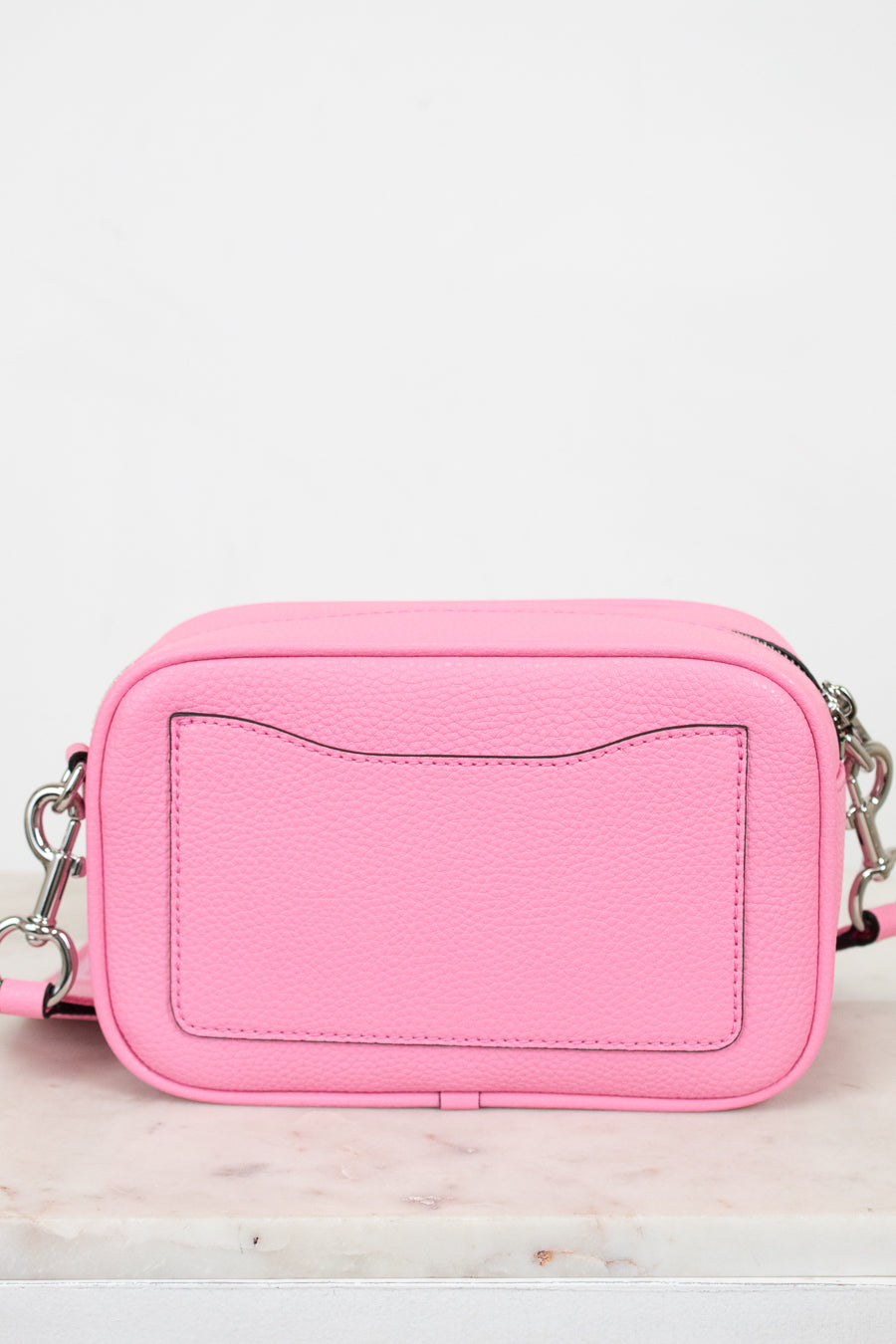 Pink crossbody bag on a light marble surface with a white background