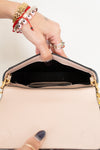 Hand opening a beige handbag with gold accents on a light background