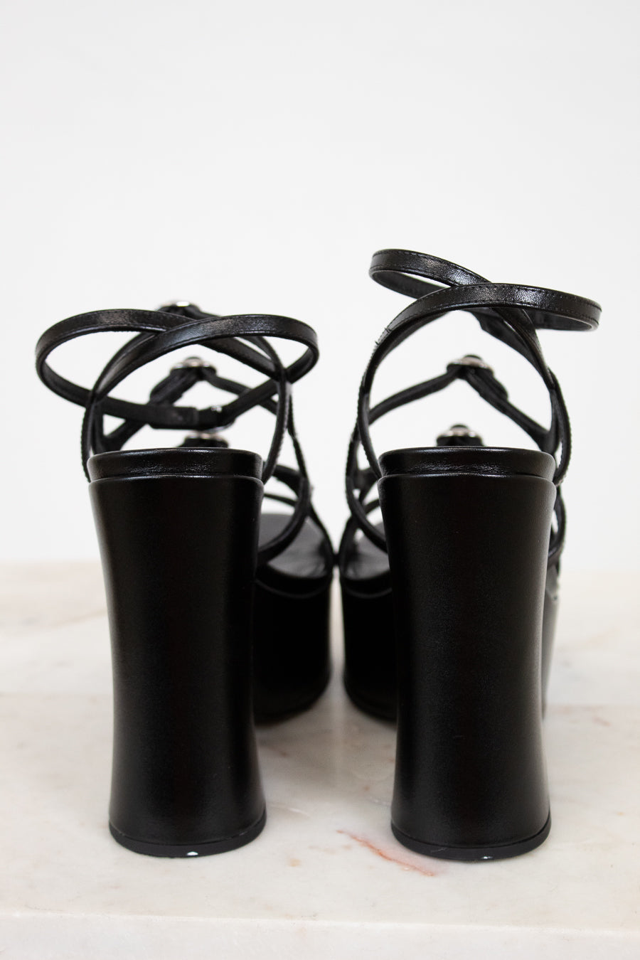 Black high-heeled shoes with strappy design on a white background