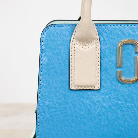 Blue handbag with beige handle and gold logo on a light background