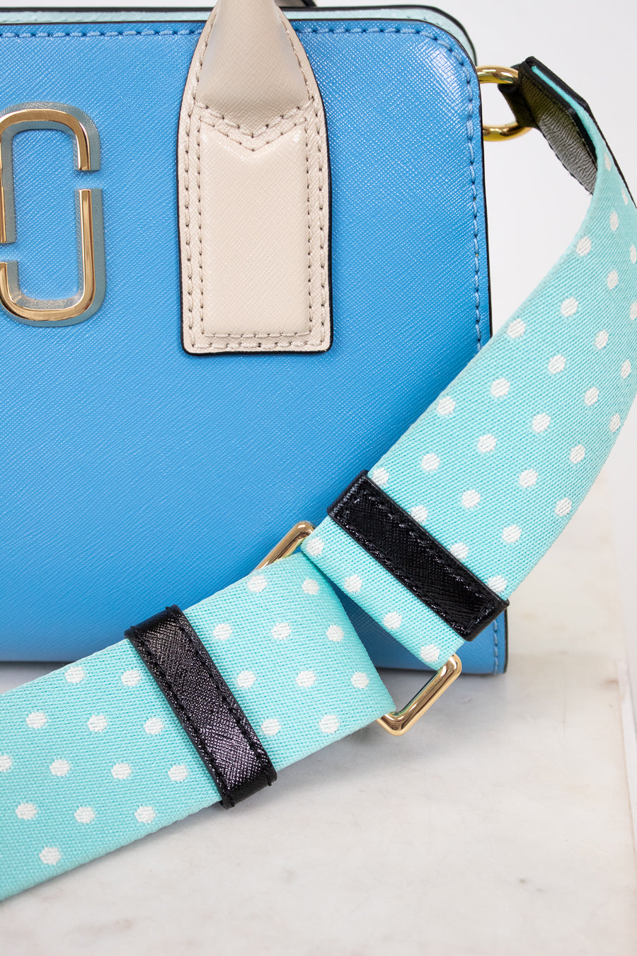 Blue handbag with a polka dot strap on a light background
