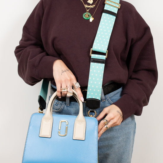 Person holding a blue handbag with a turquoise strap against a plain background