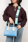 Person holding a blue handbag with a turquoise strap against a plain background