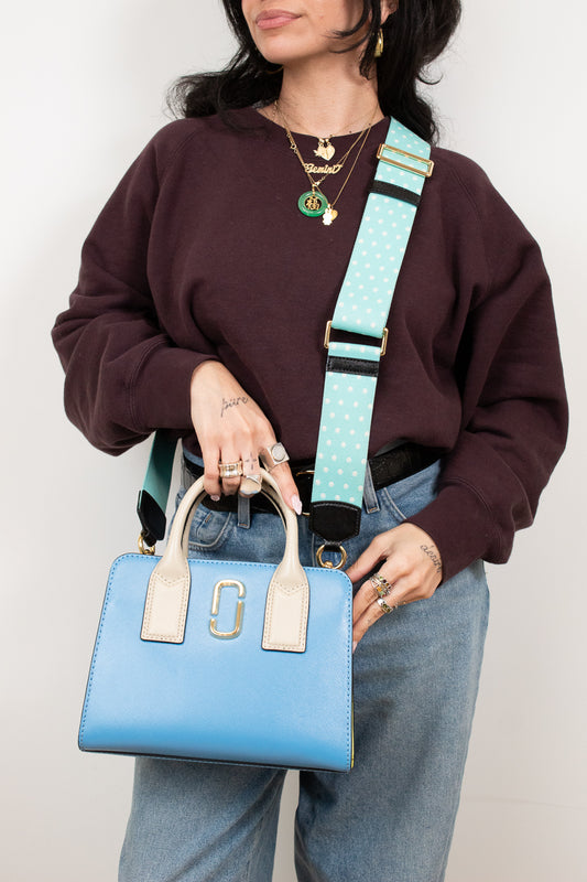 Person holding a blue handbag with a turquoise strap against a plain background