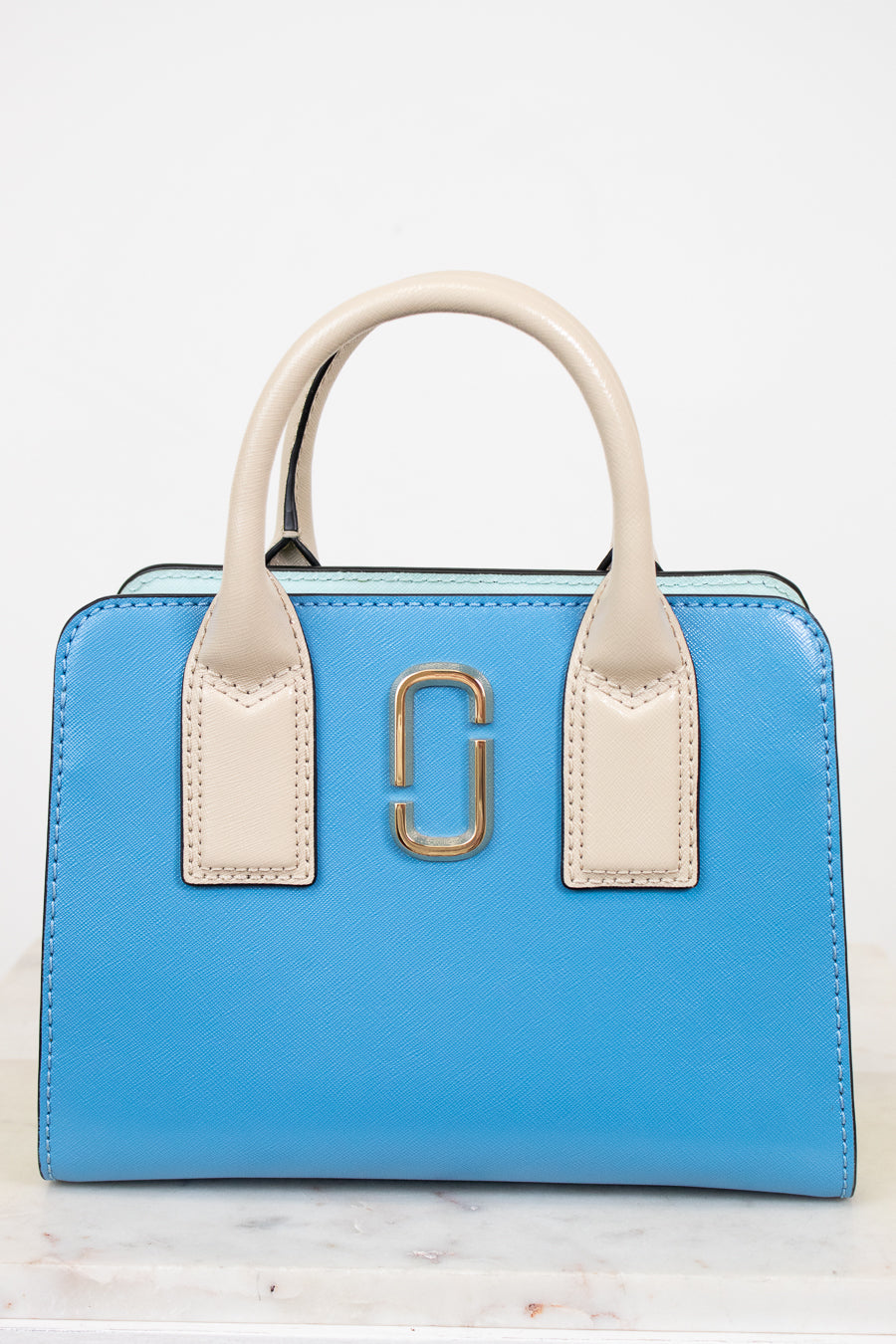 Blue handbag with beige handles and gold clasp on a white background