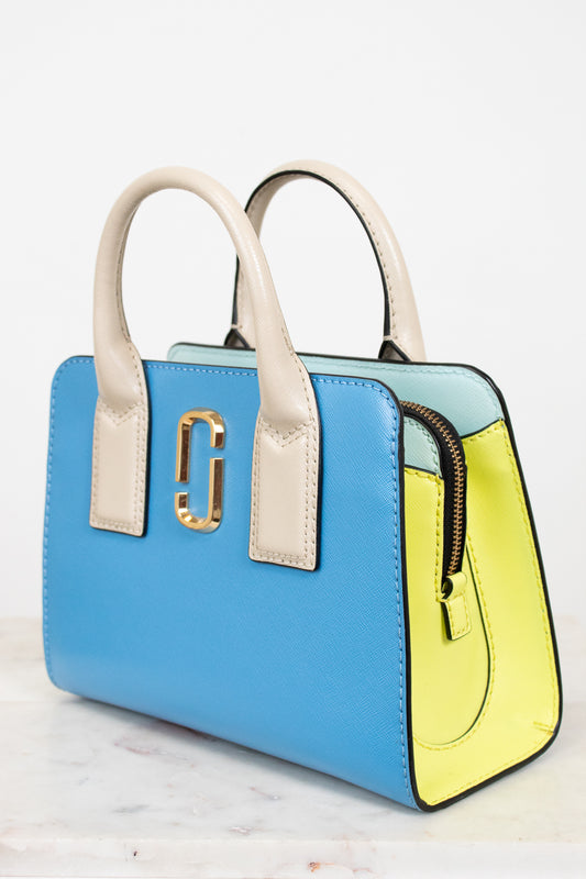 Color-blocked handbag with blue, yellow, and beige sections on a white background