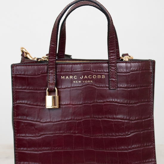 A Marc Jacobs New York crocodile-embossed leather handbag in deep burgundy, featuring dual top handles, a gold-tone padlock detail on the front, and gold branding lettering.