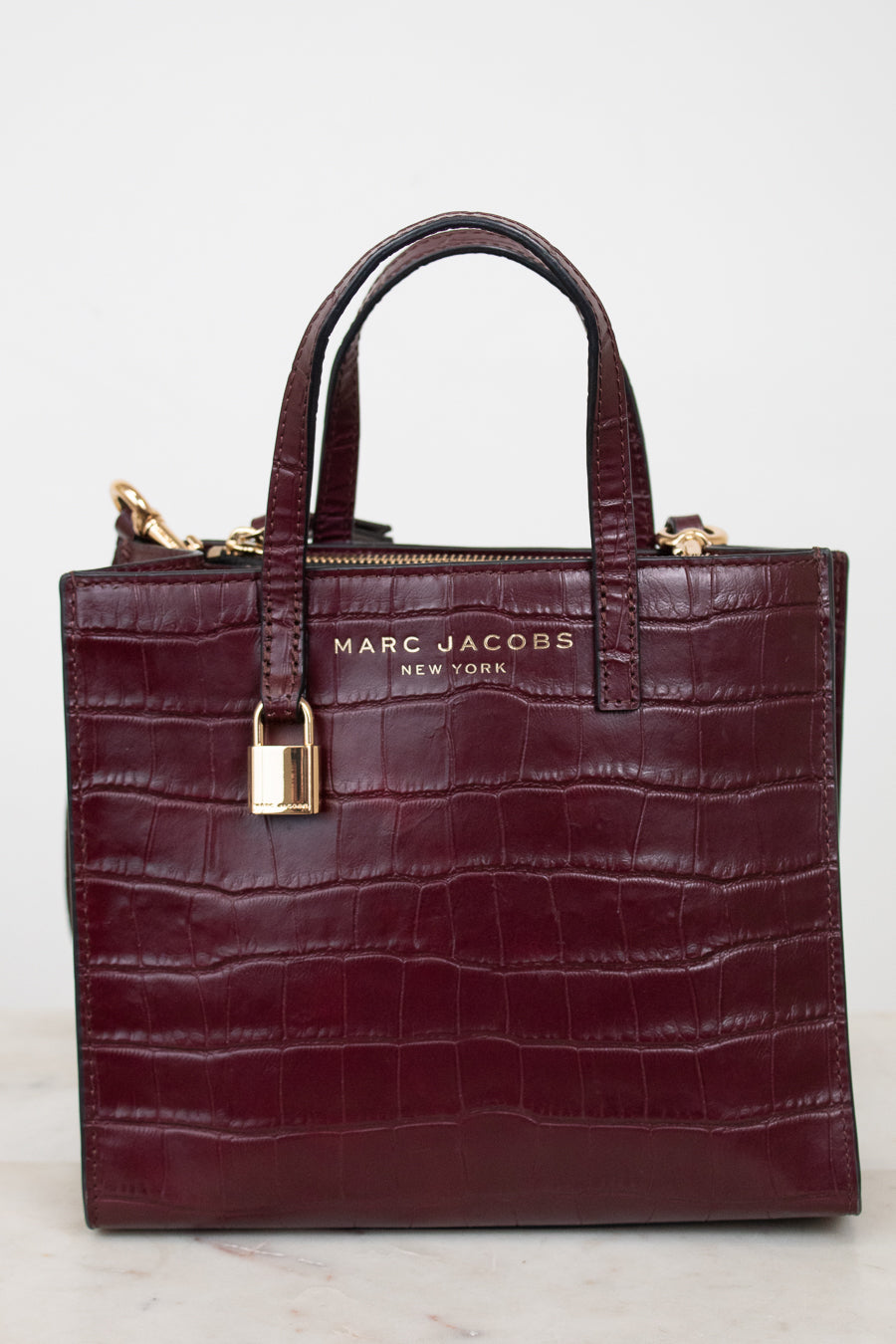 A Marc Jacobs New York crocodile-embossed leather handbag in deep burgundy, featuring dual top handles, a gold-tone padlock detail on the front, and gold branding lettering.