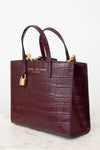 A Marc Jacobs New York crocodile-embossed leather tote bag in deep burgundy, featuring dual top handles, gold-tone hardware, and a gold brand plaque on the front, set against a clean white background.