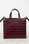 A structured burgundy crocodile-embossed leather handbag with double top handles and gold-tone hardware, displayed on a light marble surface against a white background.