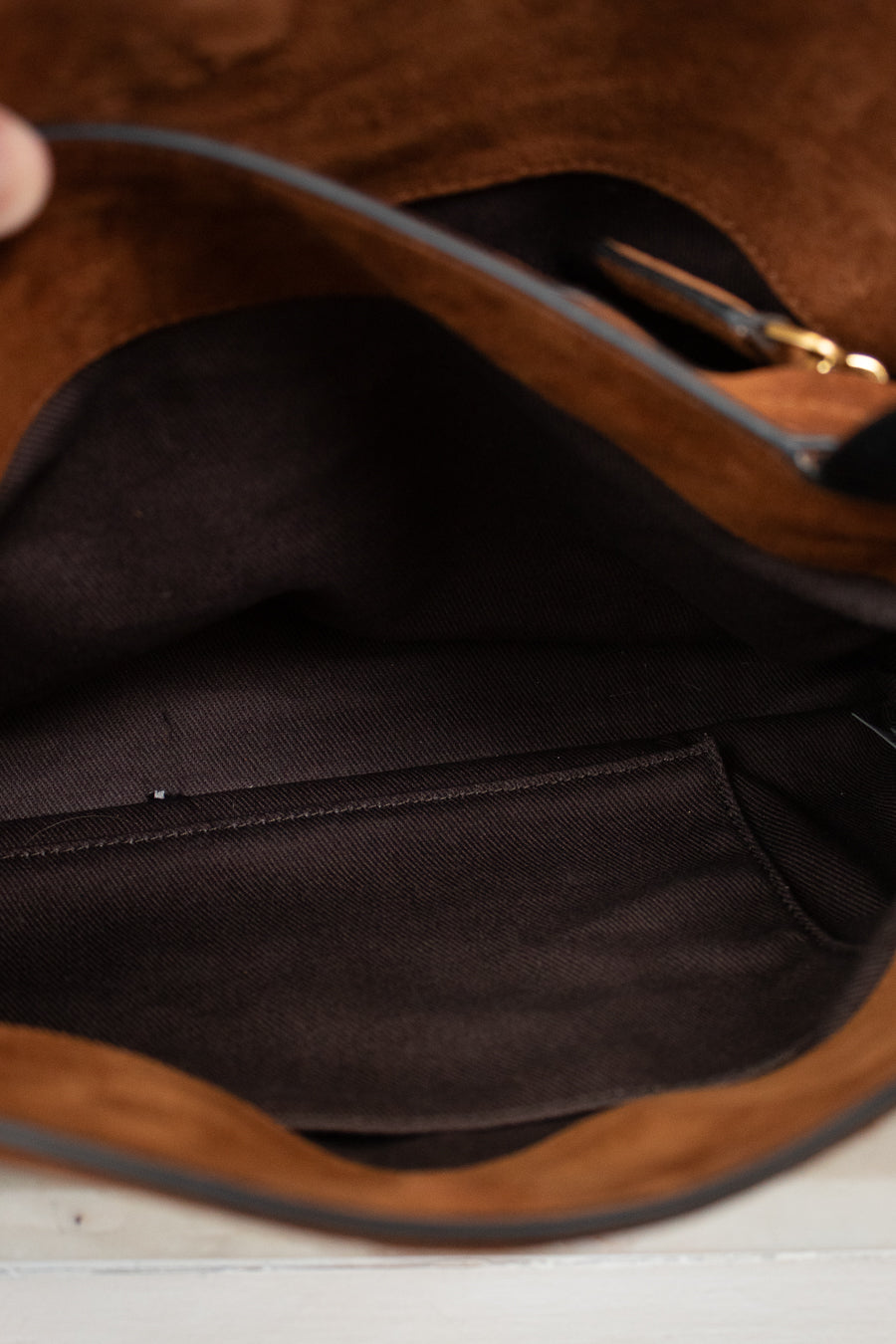 Close-up of the interior of a brown suede or faux-suede handbag, showing a black fabric lining, interior pocket, and a small gold zipper pull.