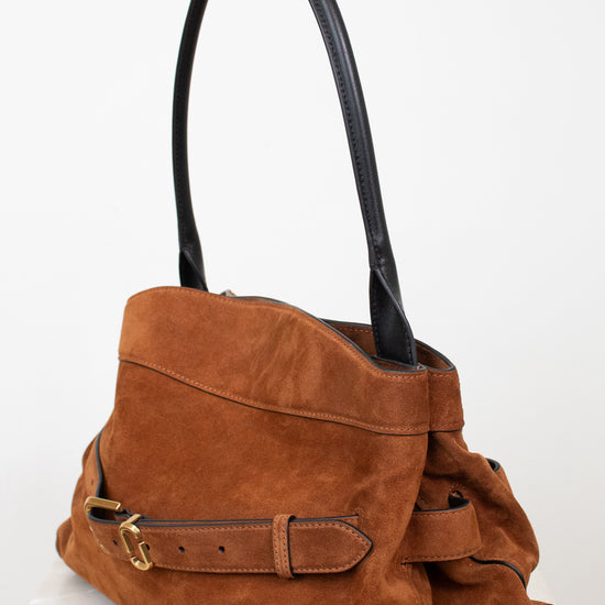 A brown suede shoulder bag with black leather handles and a matching brown leather strap detail with gold-tone hardware, displayed on a white marble surface against a white background.