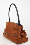 A brown suede shoulder bag with black leather handles and a matching brown leather strap detail with gold-tone hardware, displayed on a white marble surface against a white background.