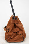 A brown suede bucket bag with black leather trim, a black shoulder strap, and a brown leather strap detail on the side, photographed against a plain white background.