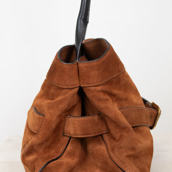 A brown suede bucket bag with a black leather strap and trim, shown against a plain white background.