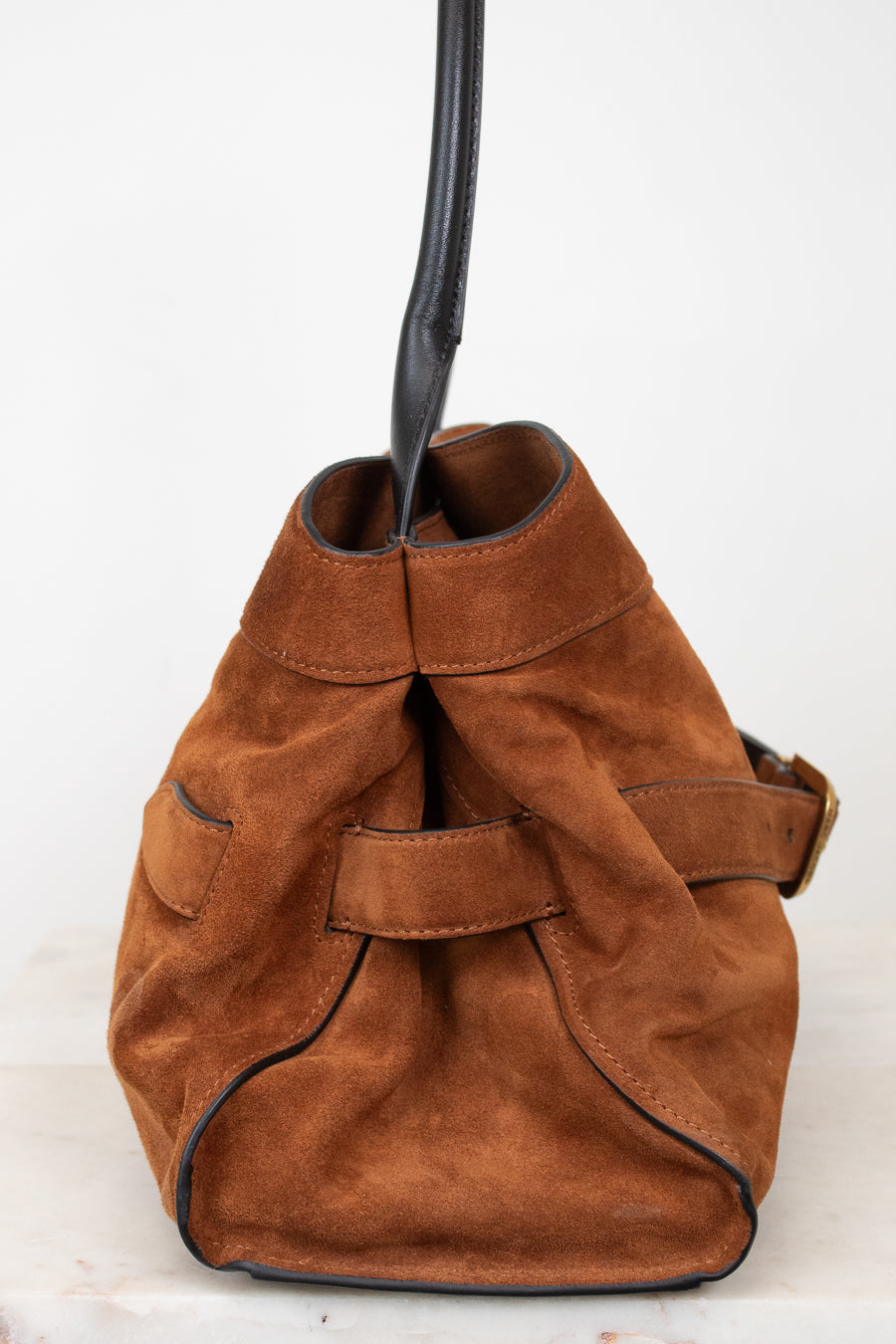 A brown suede bucket bag with a black leather strap and trim, shown against a plain white background.