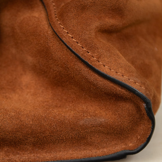Close-up of a brown suede or nubuck bag corner with visible black piping along the edge, resting on a light marble surface.