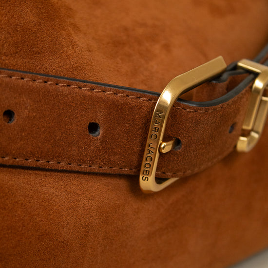 Close-up of a brown suede belt with a gold-tone Marc Jacobs buckle, attached to a matching brown leather strap on a brown suede bag.