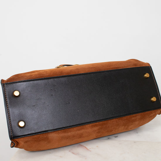 A close-up of the bottom corner of a brown suede and black leather handbag, showing gold-tone metal studs on a white marble surface against a white background.