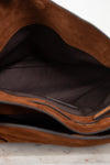 Close-up of the interior of a brown suede or faux-suede bag, showing a dark brown fabric lining and a zipper edge on a light surface.